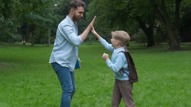 Image of a modern beard father giving a hi-five his little son in the park. Dad meets his son from elementary school. the end of the school day concept.