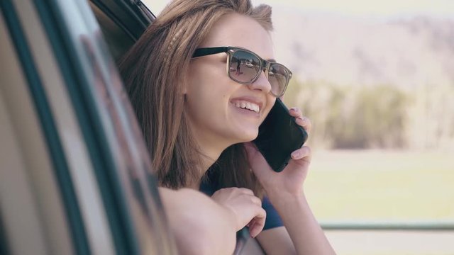 attractive smiling lady with modern smartphone looks out of open automobile window on sunny day extreme close view