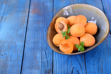 Ripe apricots in a ceramic bowl on the blue table