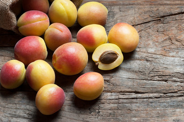 Fresh whole Ripe apricot fruits with a leaf and half in burlap sack on wooden rustic table. Apricots healthy fruit background
