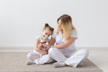 family and pets concept - mother and child daughter sitting on the floor with puppy Jack Russell Terrier on white room background