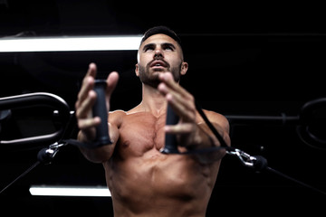 Fit and muscular man trains pectoral muscles on a block simulator in the gym.