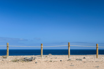Natural marine landscape with amazing blue water near El Coralejo Fuerteventura Canary Island Spain. Summer exotic vacation postcard from a tropical island in the ocean. Row of wooden posts with rope.