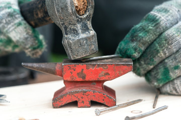 Worker is straightening a nail by hammer on a anvil on his workbench.