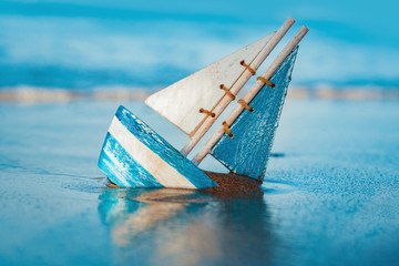 wooden toy sailboat buried into sand near the seashore