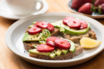 Sandwich with avocado and strawberry with whole grain bread on a plate, wooden table background