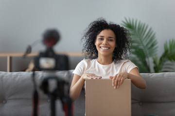 Happy african young woman blogger open parcel shooting video blog