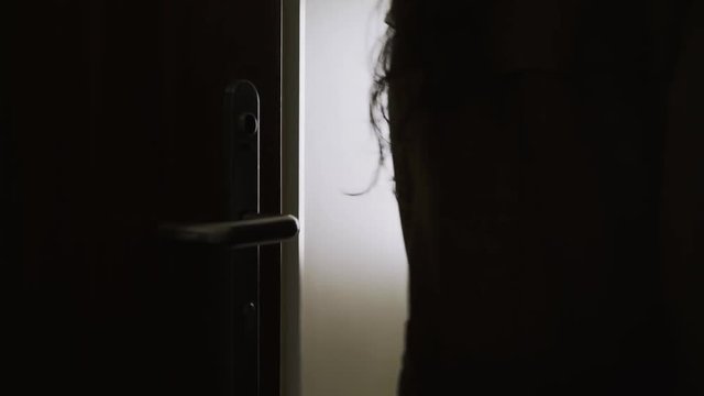 Back view woman opening door and entering in hotel apartment. Detail female hand holding door handle. Girl in coat moving inside room with trolley bag. Concept of comfortable vacation 
