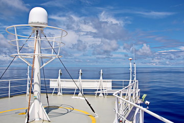 Blue sky and clouds in the open ocean. Views of the ship's mast and antennas on the navigation deck.