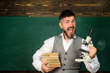 Education, research, knowledge, technology. Happy male teacher holds books and microscope. Student doing research using microscope. Scientist, docent, student with books and microscope in auditorium.