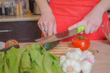 Chef cuts the vegetables into a meal. A woman uses a knife and cooks. Woman's hands cutting vegetables, behind fresh vegetables