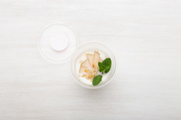 Yogurt pear slices and mint and pine nuts lie in a lunch box on a white table next to scattered with pine nuts and pear slices. Healthy eating concept. Copy space