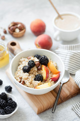 Oatmeal porridge with fruits, berries and honey in a bowl, cup of coffee with milk on background....