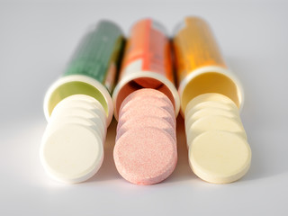 Three kinds of soluble effervescent vitamins spilled out of plastic bottles on a white background. Under a sunlight. Vitamins and nutritional supplements. Health care and medical.