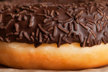 Part of a chocolate-coated doughnut with chocolate sprinkles. On parchment. Close up