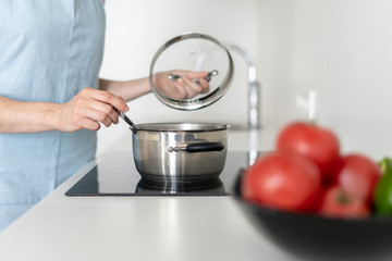 Woman cooking food in saucepan, using built in electric stove