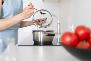 Woman cooking food in saucepan, using built in electric stove