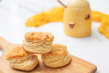 Three homade biscuits stacked on a wooden cutting board on a white marble countertop.  Yellow honey pot in background