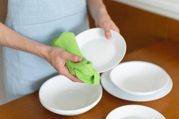 Woman cleaning plates and bowls on kitchen with wooden table
