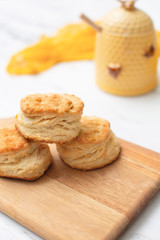 Three homade biscuits stacked on a wooden cutting board on a white marble countertop.  Yellow honey pot in background