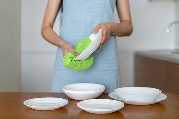 Woman cleaning plates and bowls on kitchen with wooden table