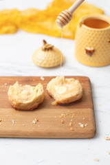 Homemade biscuit on cutting board with yello honey pot in background.  Honey drizzled onto biscuit.