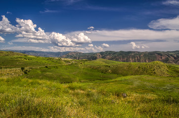 View of the highway with a turn leading to the Garni temple among the mountains of Geghama ridge in Armenia against the blue sky covered with huge clouds