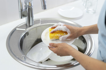 Woman using sponge with foam, washing plate in sink at white kitchen