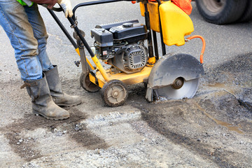 The worker starts the engine of the gasoline cutter to cut and clear bad asphalt on the roadway.