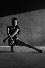 Beautiful sensual woman in black body suit posing in the studio with beautiful sunlight over grey concrete walls background - black and white photo