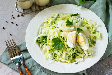 Healthy salad. Vegan salad with cabbage, eggs, cucumber, coriander and mayonnaise-mustard dressing on a light stone or slate table. Free space for your text.