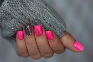 The  pink manicure with the knitted sleeve of a grey sweater on grey background. Winter concept.