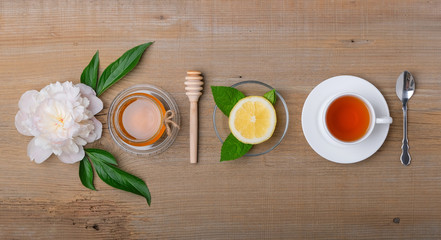 A cup of tea, lemon, a jar of honey on a wooden background.