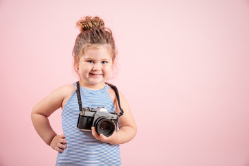 Fototapeta premium Little girl holding old vintage camera and smiling on pink background