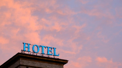Weathered and burned out neon hotel sign lit up against a colorful and dramatic red and orange sky...
