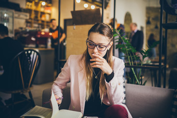 theme modern profession for young women. beautiful girl with glasses sitting at wooden table inside cafe. hand with pen makes entry in notebook diary. Man uses paper reminders and schedules