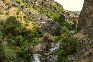 View of the basalt slopes and the Azat river flowing in summer, among the bushes and trees along the banks in the Garni gorge in Armenia