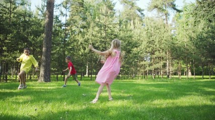 Slow motion shot of three kids having fun playing tag game on lawn in summer park. Little friends enjoying running on green grass on sunny days