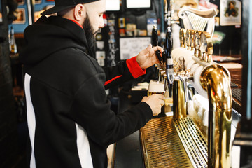 smiling barman pouring beer in a bar. Bearded courageous man pours you a foaming drink. Golden tap for draft beer