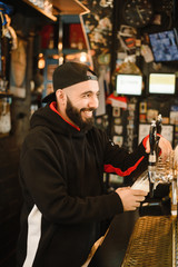 smiling barman pouring beer in a bar. Bearded courageous man pours you a foaming drink