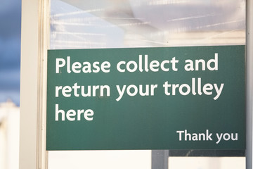 Collect and return trolley sign at supermarket shop shelter store