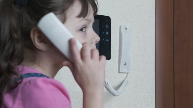 The child picks up the doorphone. The child is alone at home. A little girl without parental supervision talks on the intercom and presses the buttons.