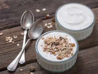 White yogurt in glass bowl with oatmeal on top on rustic wooden desk.