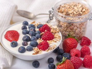 White yogurt in bowl with oatmeal and strawberries, blueberries and raspberries on the top on white background.