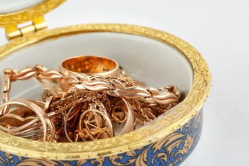 Small ceramic box with gold jewelry in it on white background, macro
