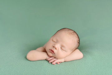 Sleeping newborn baby on a green background. Photoshoot for the newborn. A few days from birth.