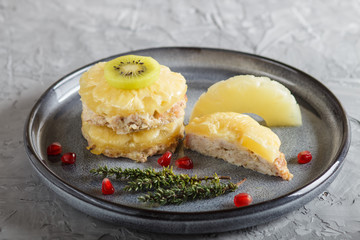 Pieces of baked pork with pineapple, cheese and kiwi on gray plate.