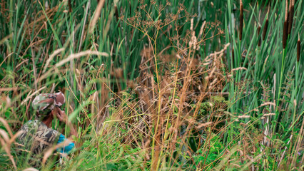 Fisherman fishing on lake. Fisherman sitting in grass, bulrush, cattails and smoking. man in khaki cloth.