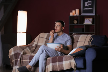 Handsome young man eating unhealthy food while watching TV at night