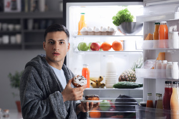 Afraid man caught in the act of eating unhealthy food near refrigerator at night